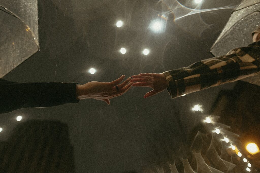 Springfield Engagement photographer captures hands reaching for each other under lights in the rain. 