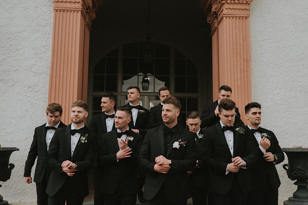 Groomsmen pose while adjusting their watches on the steps of Ravisloe Country Club during wedding portraits.