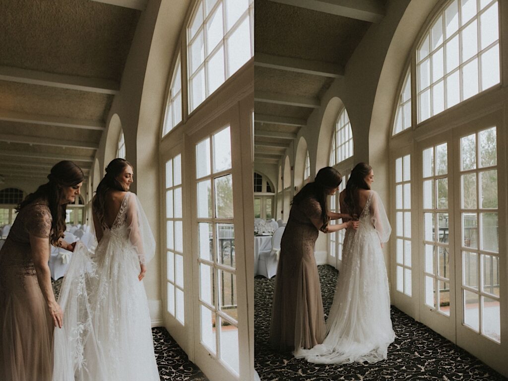 Bride's mother zips up her lacy wedding dress in front of gorgeous window before wedding ceremony. 