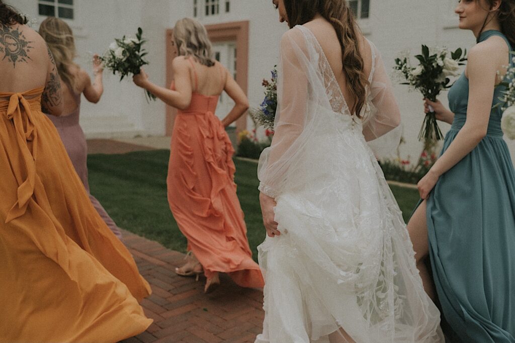 Springfield wedding photographer captures bottom half of bride and colorful bridesmaids dresses as they walk along brick path. 