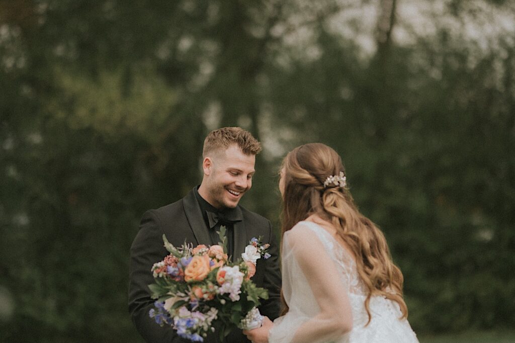 Groom smiles as he turns around and sees bride for the first time with trees in the background. 