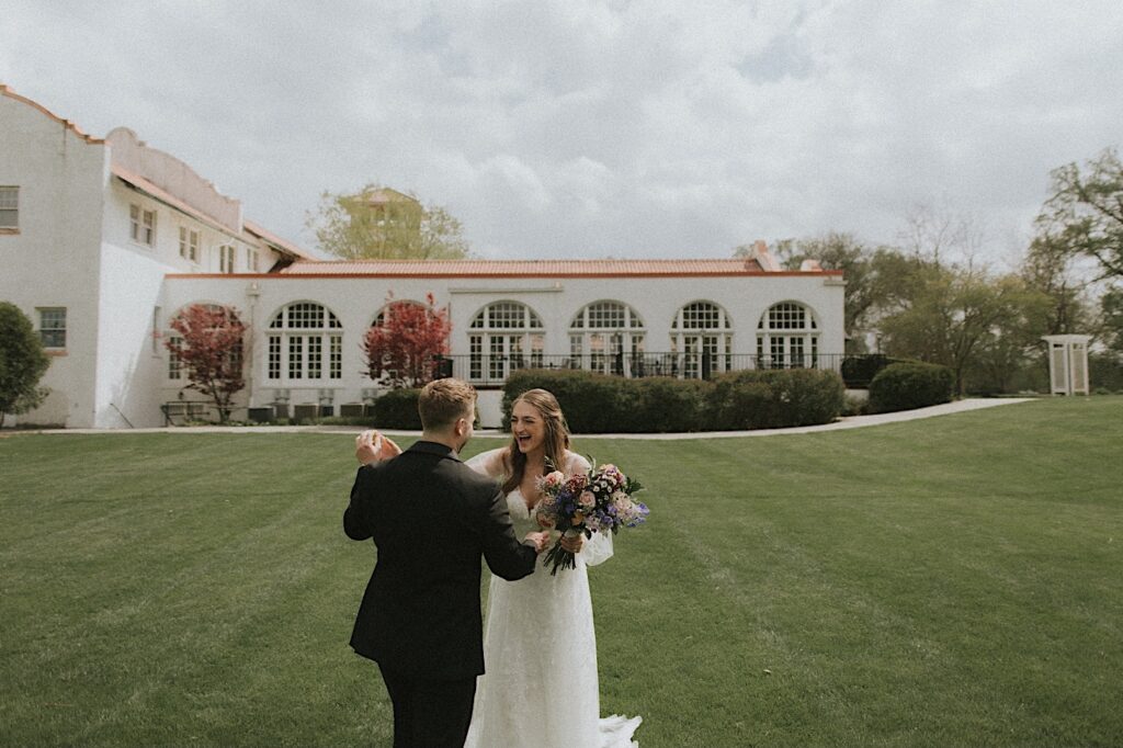 Bride and groom smile and dance in grassy field with Ravisloe Country Club in the background. 