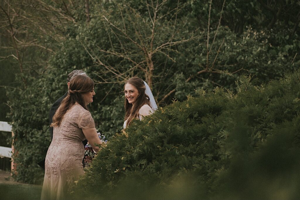 Bride is hidden behind a bush with her mom before walking down the aisle to the ceremony. 