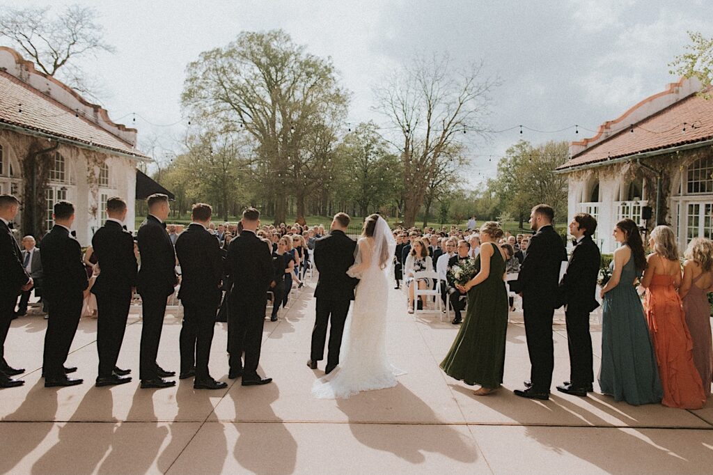 Homewood Wedding Photographer captures the back of the wedding party looking towards the seated guests as they stand lined up for the wedding ceremony. 