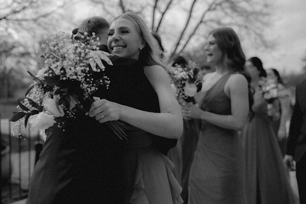 Bridesmaids hugs groom in timeless black and white photo by Chicagoland Wedding Photographer. 