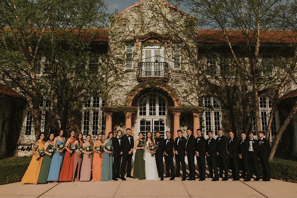 Wedding Party stands in a line and poses for Chicagoland Wedding Photographer in front of the entrance of Ravisloe Country Club. 