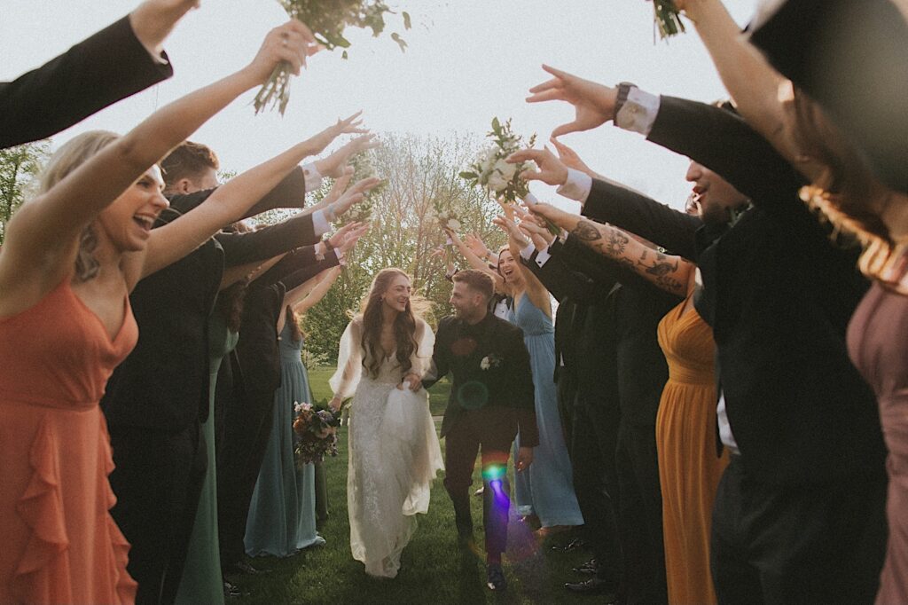 Wedding party puts their arms up to make a tunnel as the bride and groom duck down to run through it. 