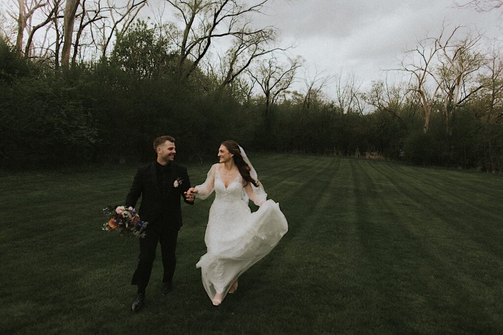 Bride and Groom run through the grass with trees behind them looking at each other. 