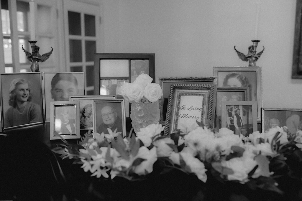 Table of photographs of family members who have passed. In the center of the table is a sign that says, "In Loving Memory" surrounded by white flowers. 