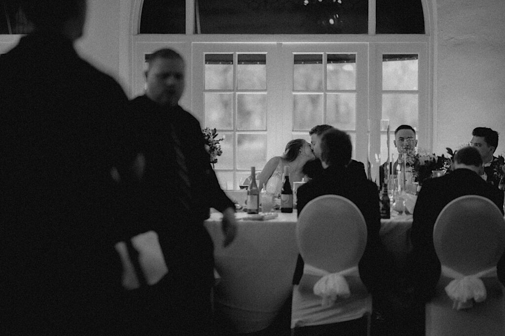 Bride and Groom sit at the head table and share a kiss during the dinner reception. 