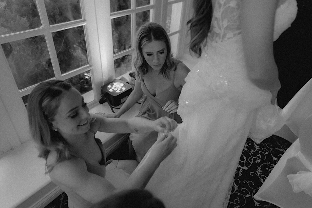 Bridesmaids kneel down to help bride bustle her dress before the wedding reception. 