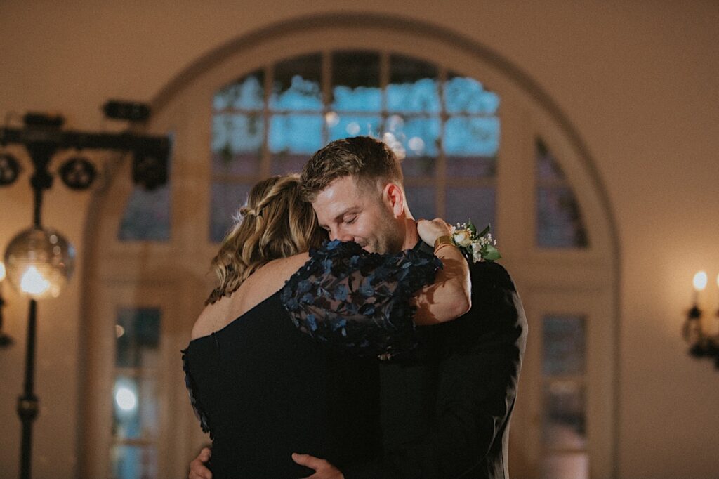 Groom closes his eye and leans his head against his mother during their dance in wedding reception hall at Ravisloe Country Club. 