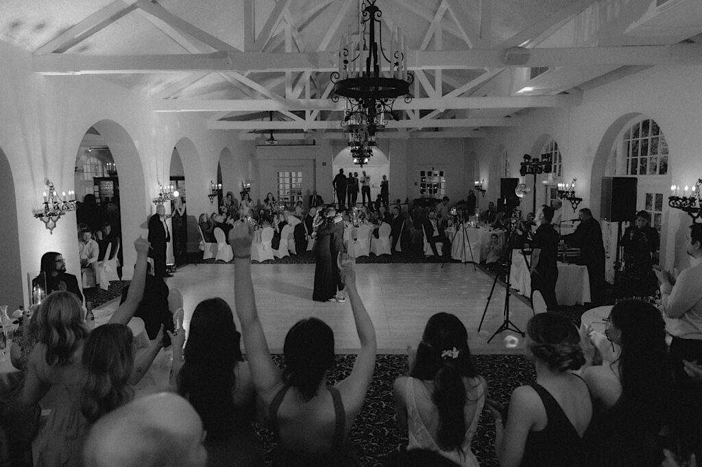 Chicagoland Wedding Photographer captures a wide shot of entire Ravisloe Country Club reception hall as wedding guests cheer on during the first dance. 