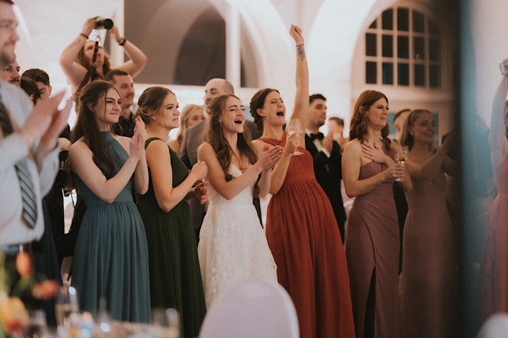 Bride stands in a line with her guests clapping and cheering during wedding reception at Ravisloe Country Club. 