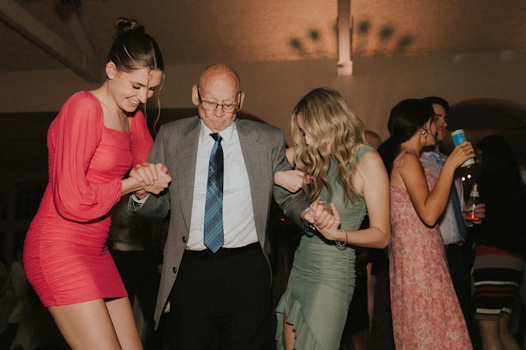 Two women in pink and green dresses help a grandfather get onto the dance floor during reception at Ravisloe Country Club.