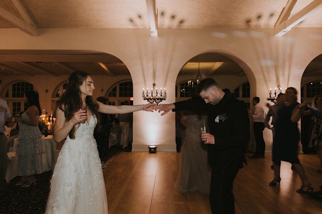 Bride and groom hold their hands out to each other on dance floor at Ravisloe Country Club reception hall. 