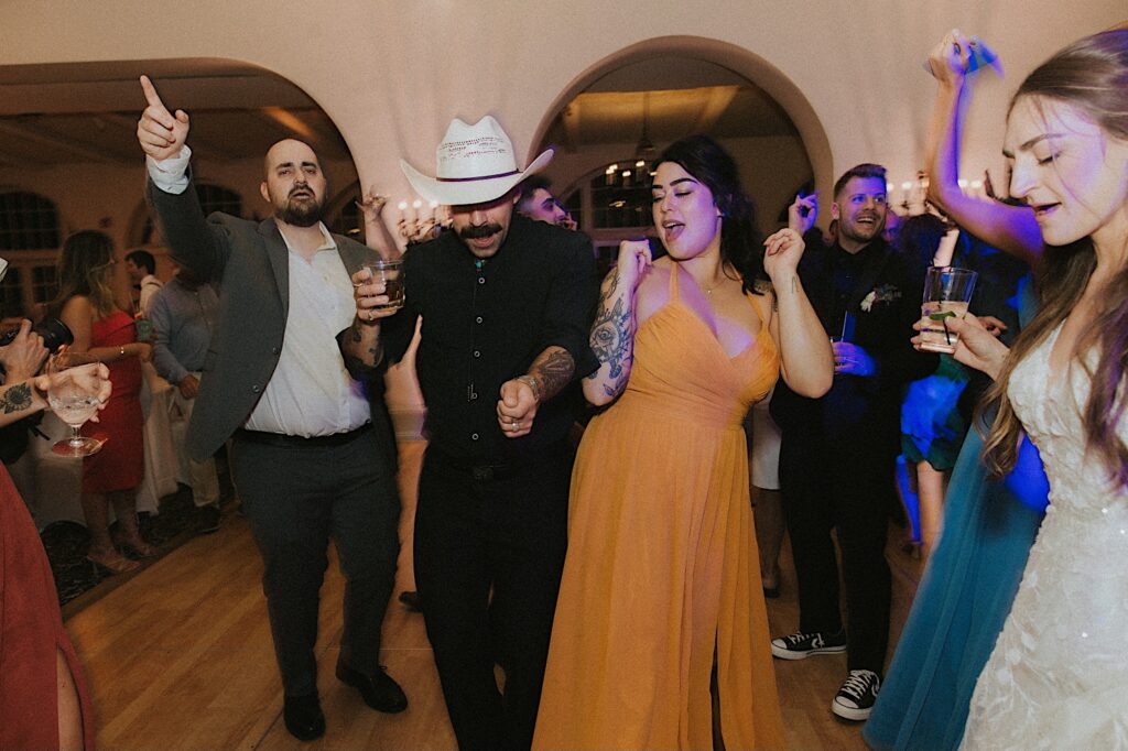 Guest in a cowboy hat dances with bridesmaid in yellow dress during wedding reception in Ravisloe Country Club hall. 