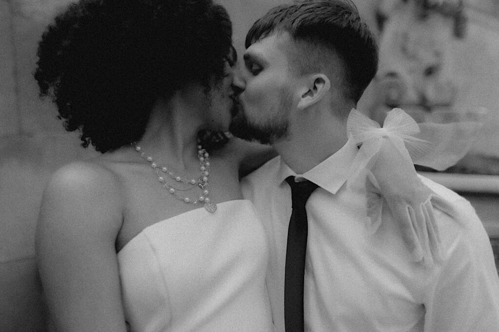 Bride and groom kiss in a romantic black and white portrait. The bride's arm is wrapped around groom showing off her sheer white gloves.