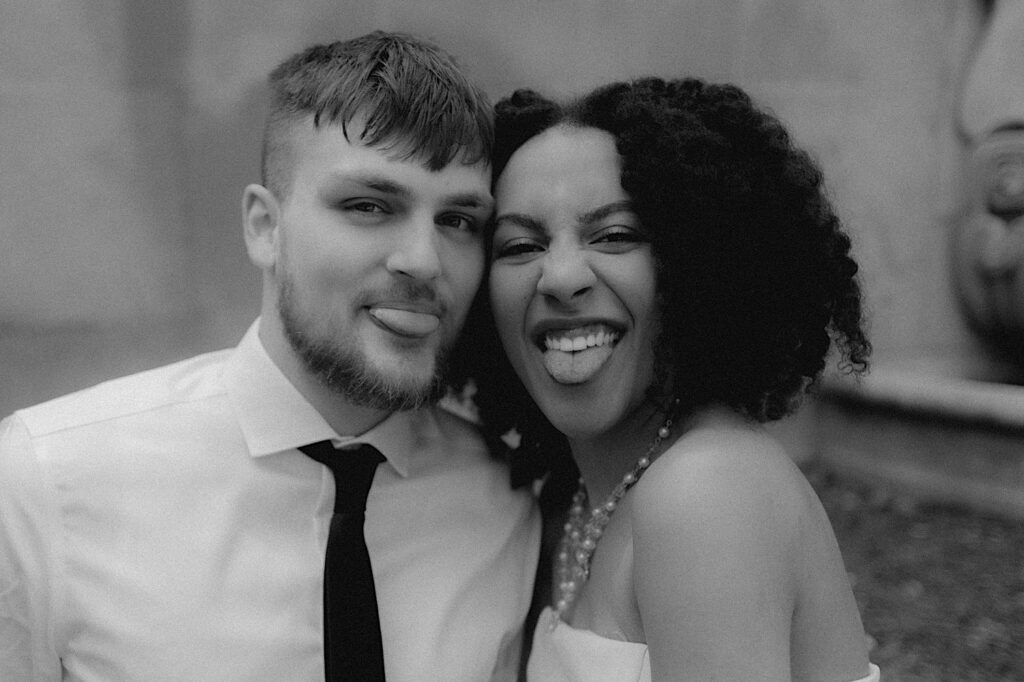 Bride and groom stick their tongues out at the camera in candid black and white elopement portrait.