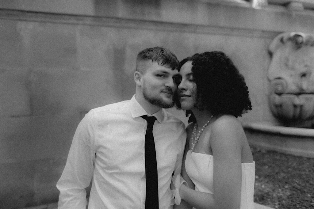 Bride closes her eyes and leans her face into grooms face as they sit on ledge outside Springfield Courthouse. 