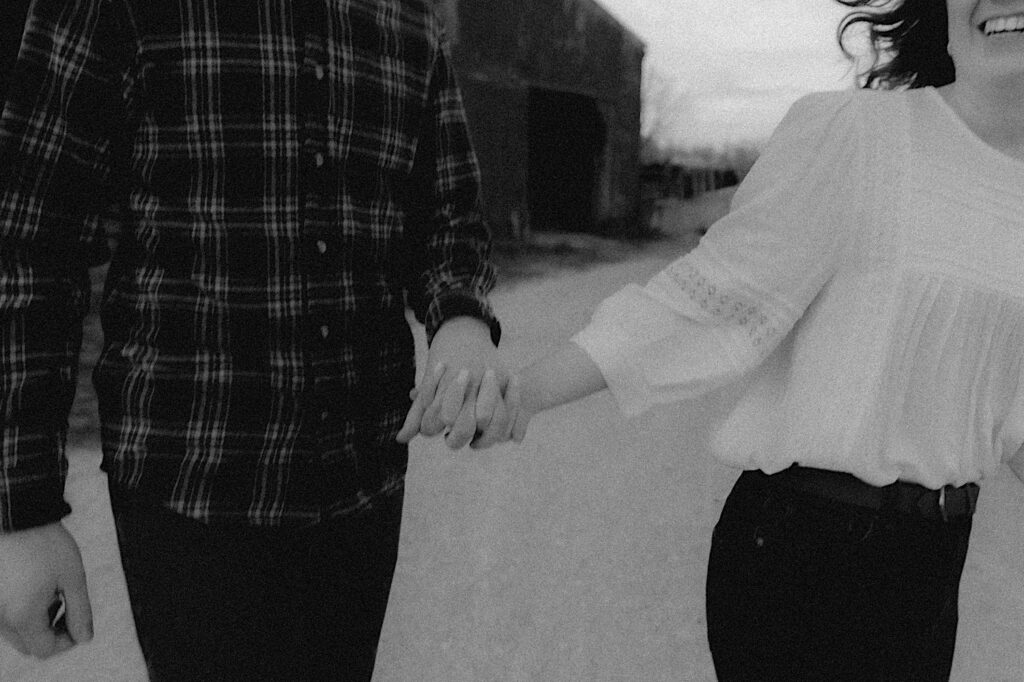 Black and White blurry film photo of couple running and holding hands between barns during farm engagement session in Central Illinois. 