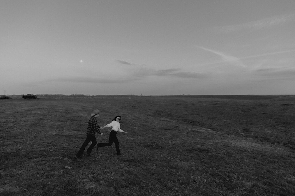 Black and White photo of couple running through grassy field on a beautiful open farm in Springfield Illinois. 