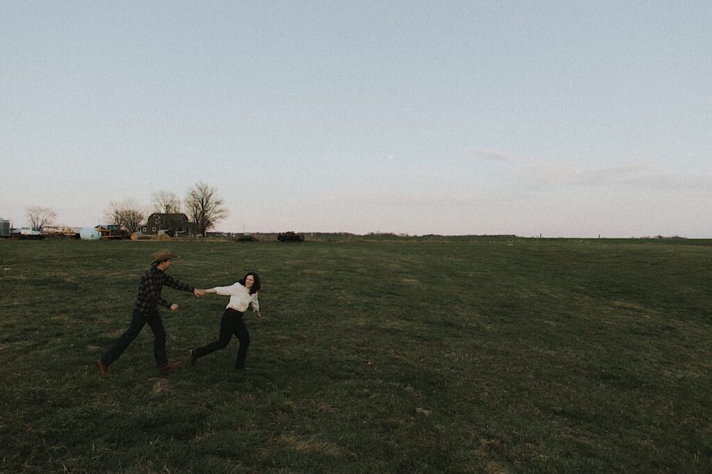 Film photo of couple running through grassy field on a beautiful open farm in Springfield Illinois. 