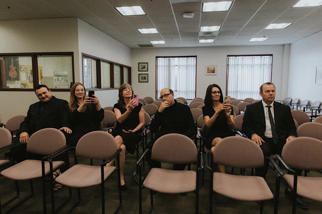 Bride and Groom's family hold up their phones while sitting in Springfield Courthouse to video Bride and Groom's elopement ceremony. 