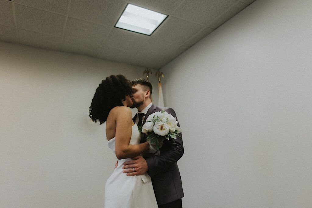 Bride and Groom kiss in courthouse room during elopement ceremony. 