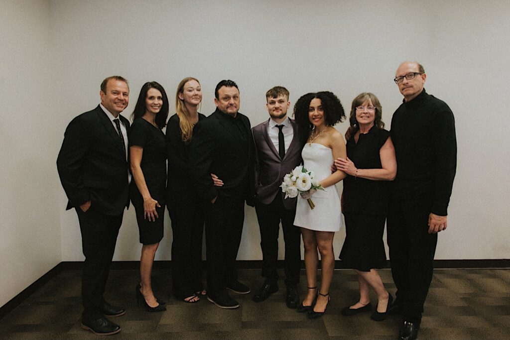 Bride and groom pose with their family in the Springfield Courthouse after elopement ceremony. The family wears all black. 