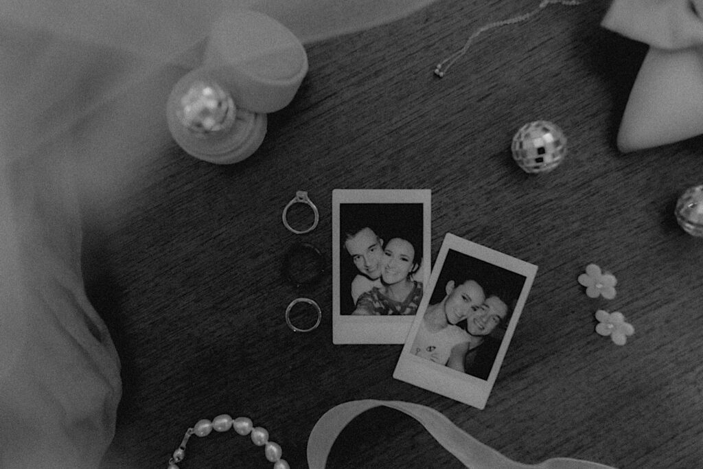 Black and white portrait of polaroids taken of bride and groom surrounded by mini disco balls and engagement rings.