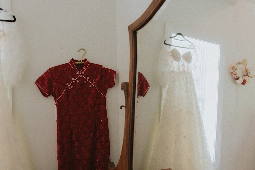 Two bridal dresses, one white and one red for hand on door in front of mirror. 