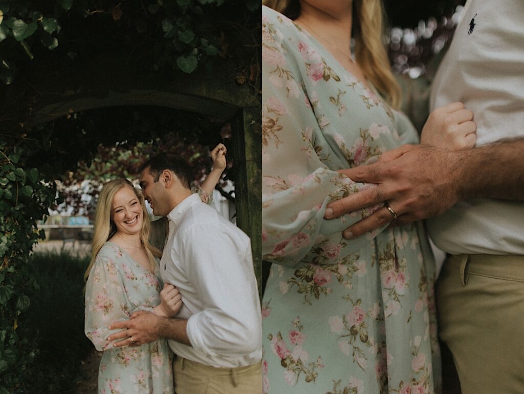 Girl in blue floral dress stands next to her partner in a white shirt underneath a greenery arch at Allerton Park. 