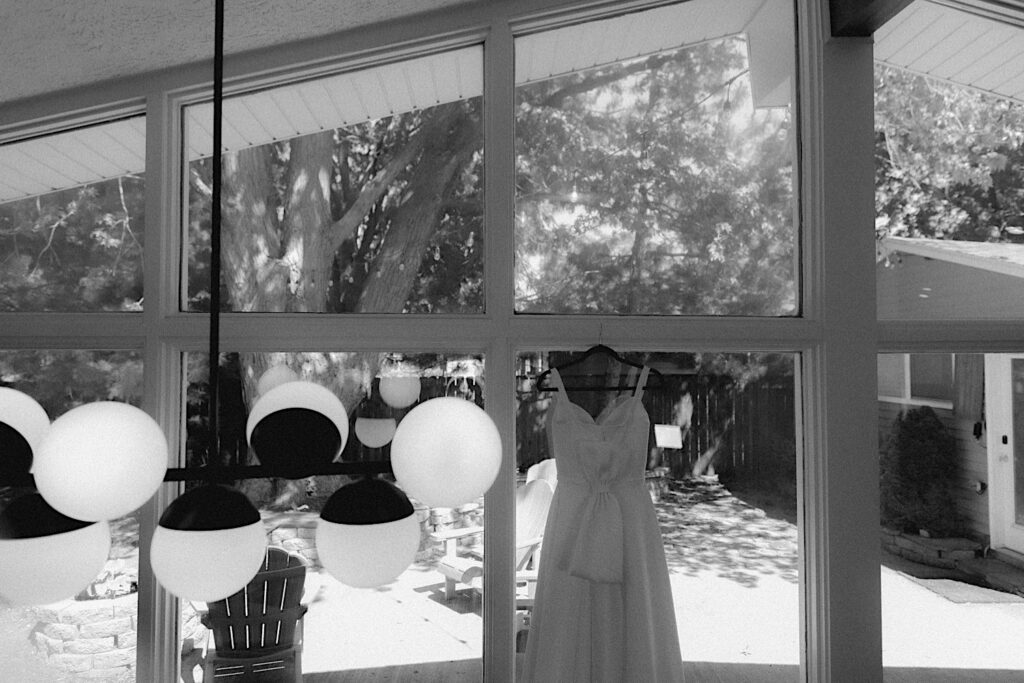 Bride's dress is hung on windowsill with a giant bow on the back. 