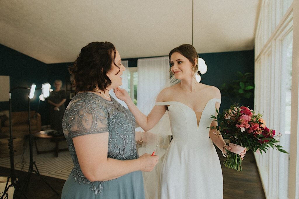 Bride touches her moms face and smiles while getting ready before wedding ceremony in Central Illinois. 