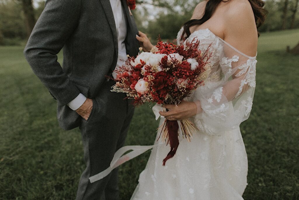 Bride reaches for groom's lapel as the Midwest wedding photographer focuses on the bride's hand holding her red and white flower bouquet. 