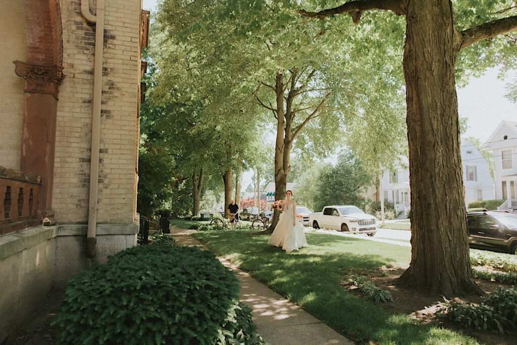 Bride stands outside Reality on Monroe underneath beautiful green trees before wedding ceremony.