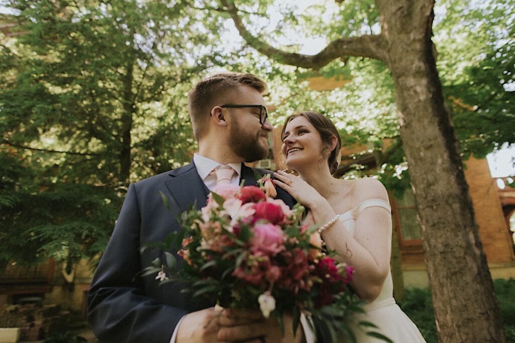 Bride puts her hands on groom's shoulders as he holds her floral bouquet in front of Reality on Monroe wedding venue. 