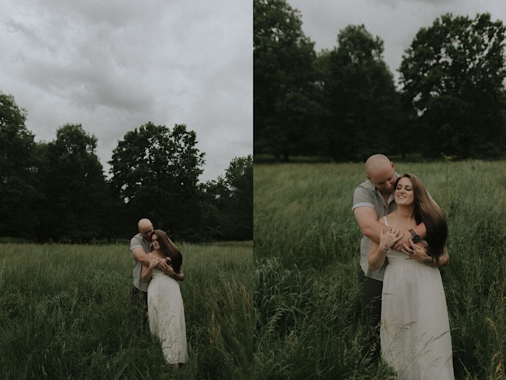 Woman leans into her fiancé who is standing behind her as they sway in a grassy plain. 