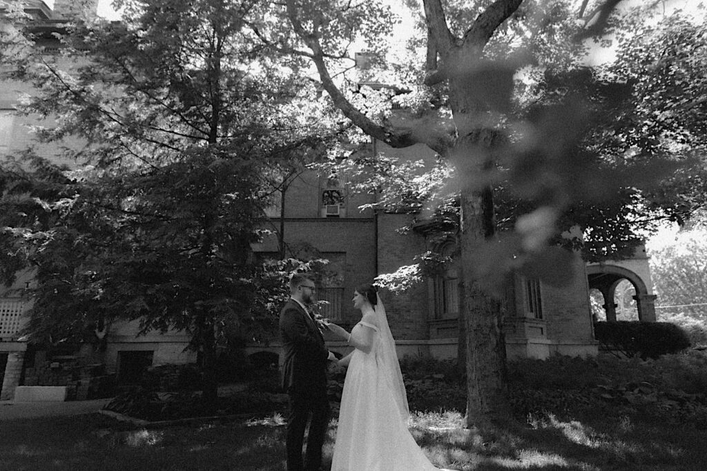 Bride reads her vows as she holds groom's hands in front of Reality on Monroe wedding venue during private vows in a black and white portrait by Central Illinois wedding photographer. 