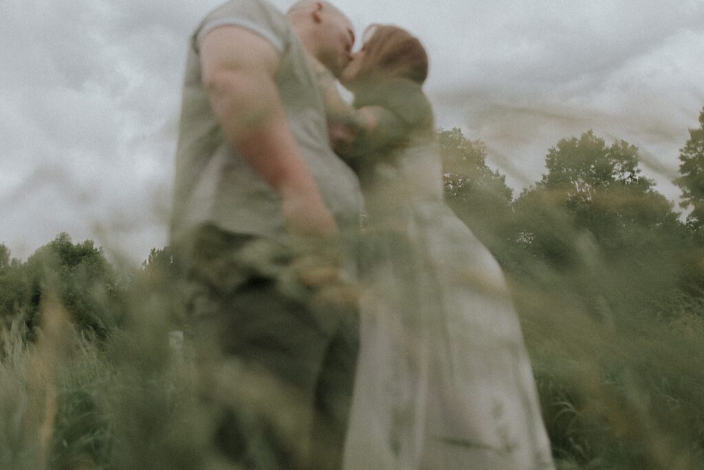 Illinois Wedding photographer captures couple kissing and hugging from underneath them with grass flowing in front of the lens.