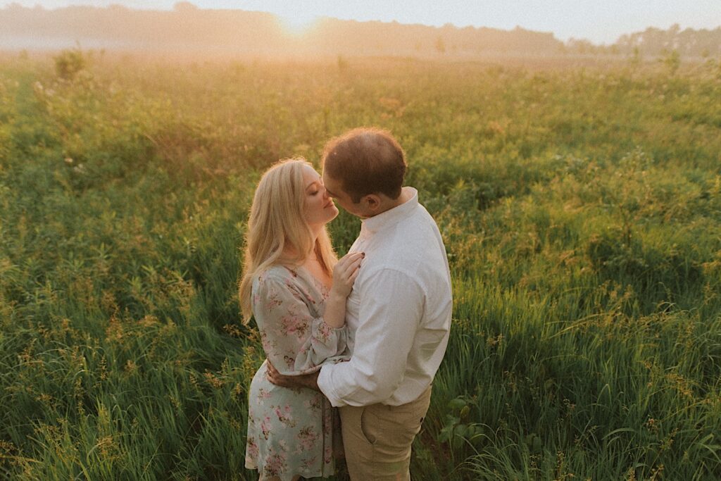 Couple leans towards each other while swaying in a green field outside Allerton Park during spring engagement session. 