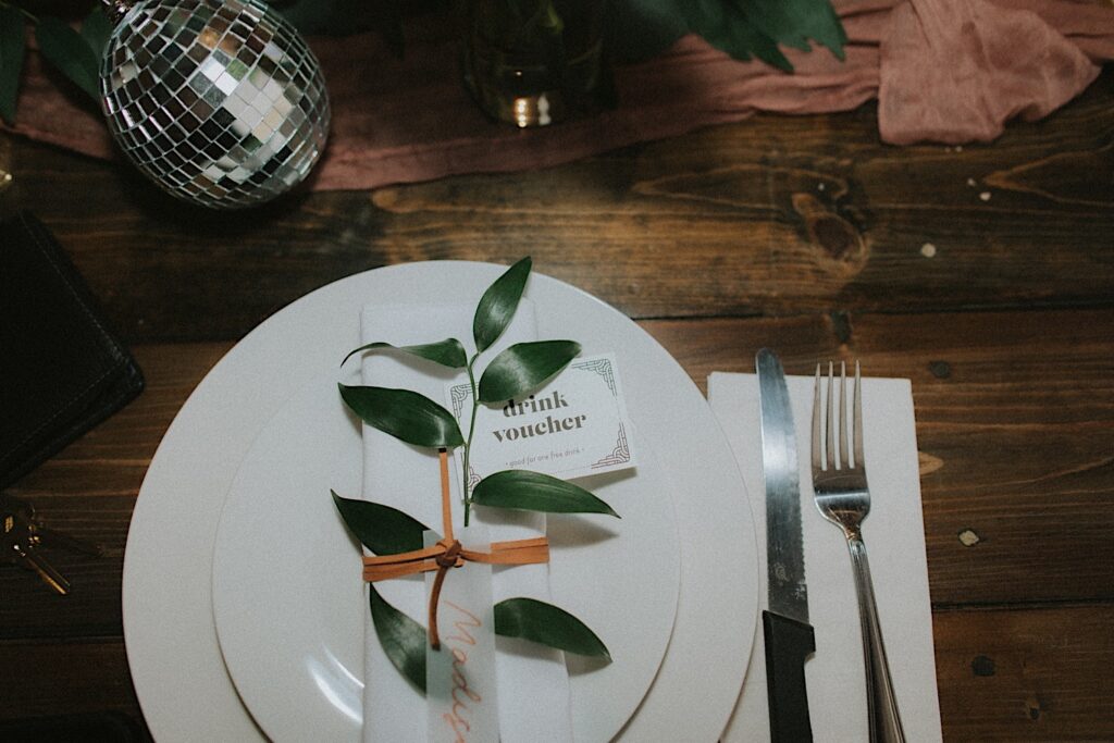 Central Illinois wedding photographer captures white plates stacked with white napkins and a leaf sitting on top of napkin tied together with an orange string. 