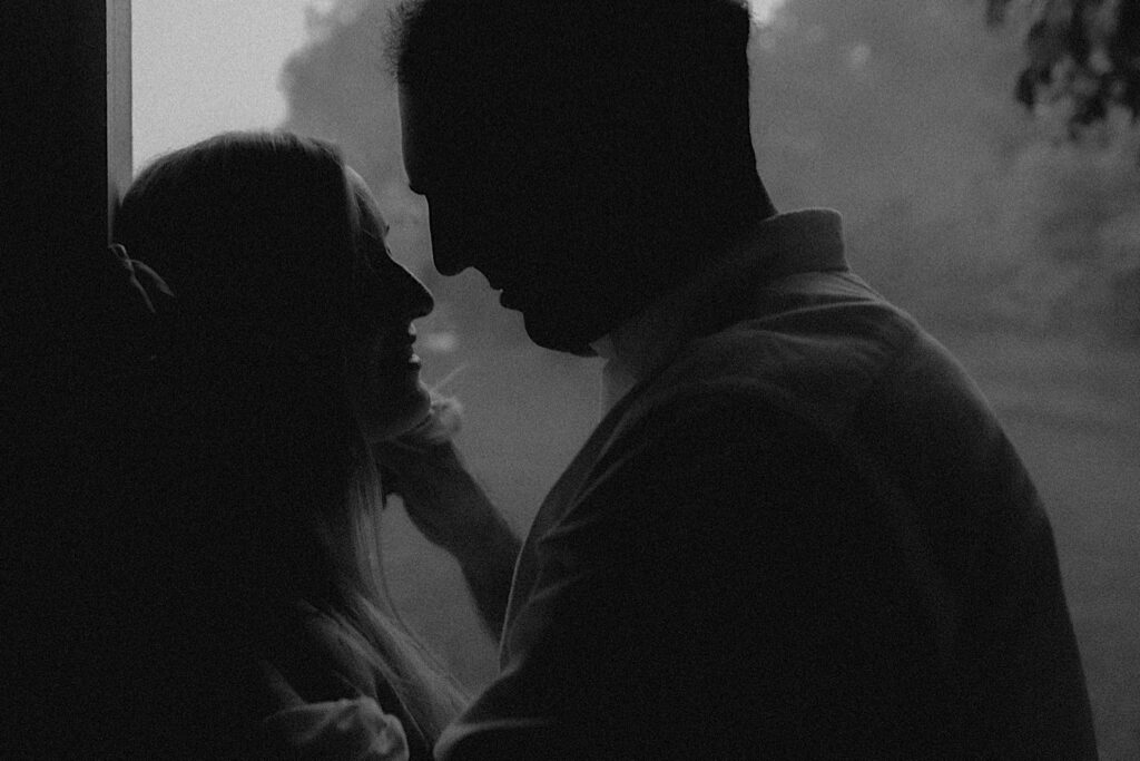 Black and white portrait of man leaning into woman for a kiss during romantic garden engagement session. 