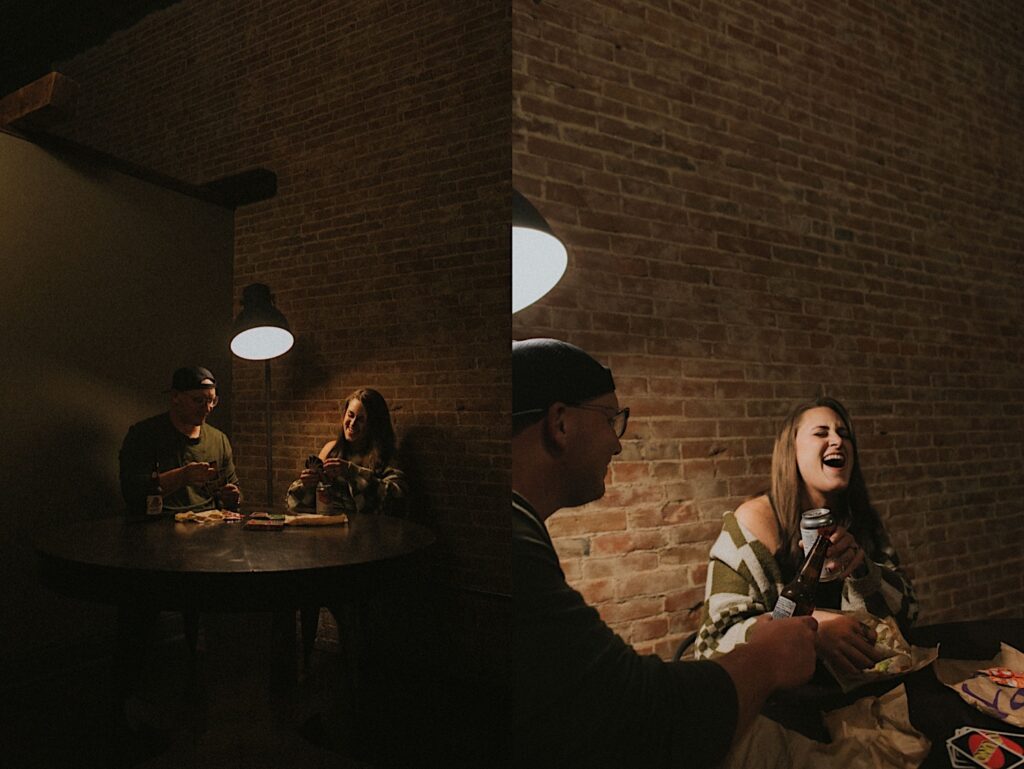 Couple sit at a table near a brick wall eating taco bell, drinking beer and laughing while playing UNO. 