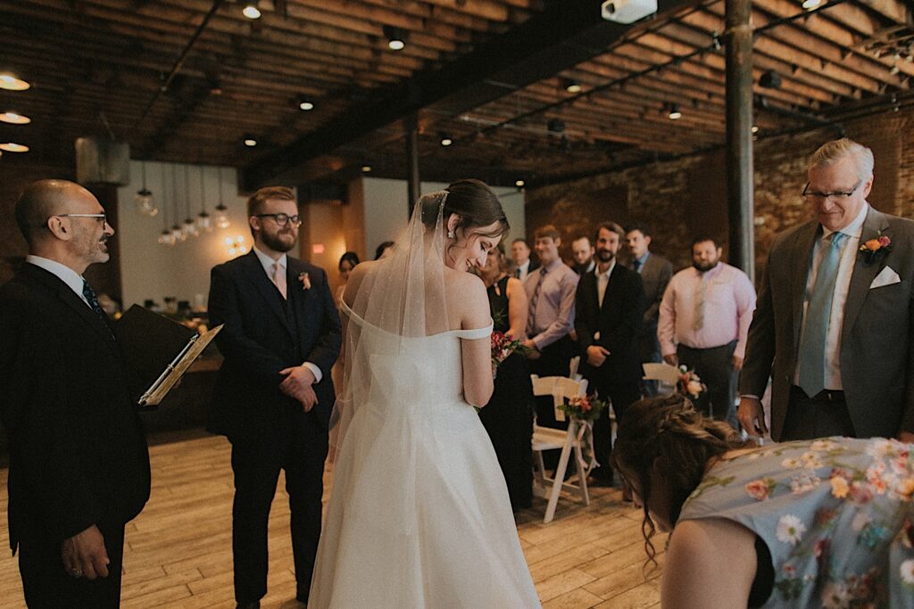 Bride looks down as her family member fixes her dress at the end of the aisle before the beginning of the ceremony in industrial room at Reality on Monroe in Central Illinois. 