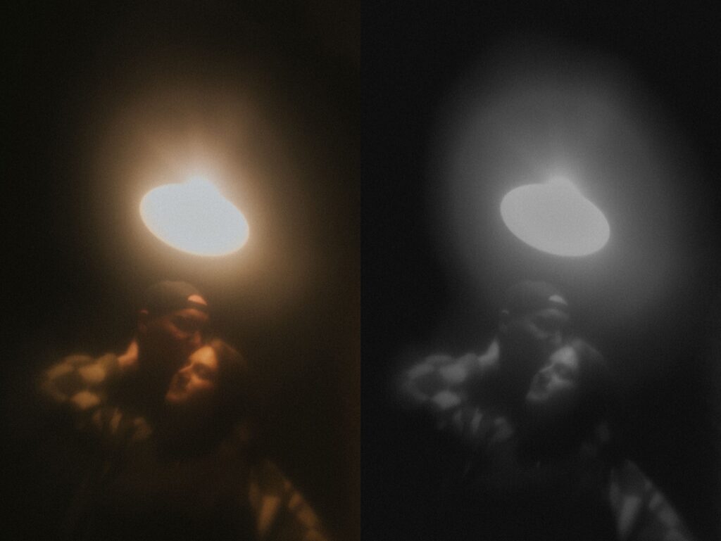 Man stands behind woman as she puts her hand on his neck and he kisses her head. The background is completely dark except for a lamp shining from above them for moody engagement portraits in Lincoln, Illinois. 