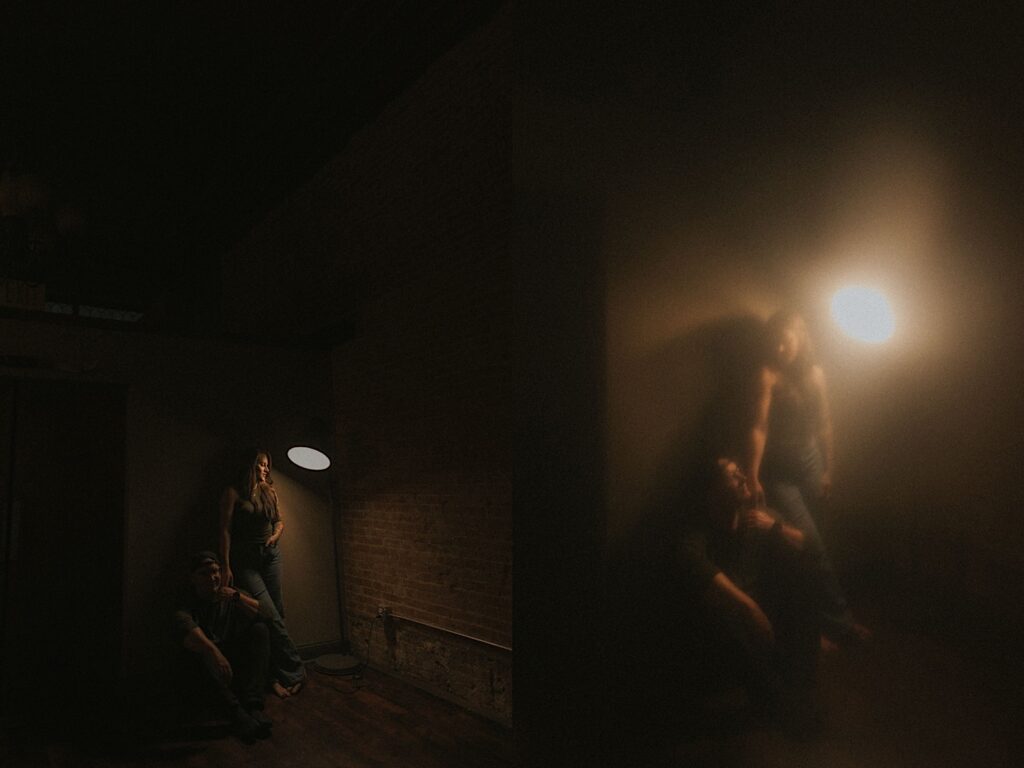 Girl leans against a wall as a man sits underneath him with a lamp shining on them and darkness around them. 