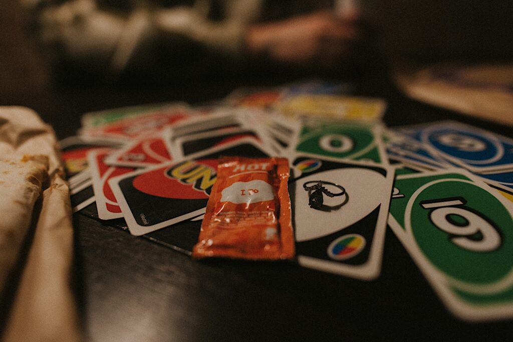 A taco bell hot sauce packet sits next to an engagement ring on a pile of UNO cards. 