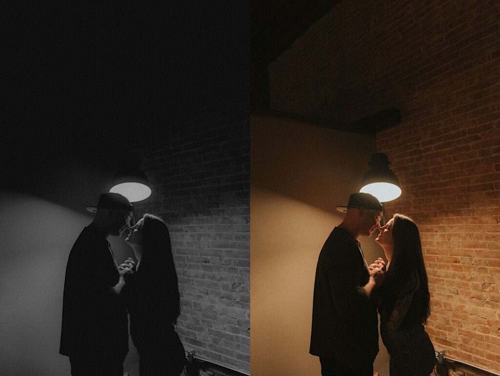 Couple poses in front of a hanging light and a brick wall for a silhouette style, moody portraits in Lincoln, Illinois. 